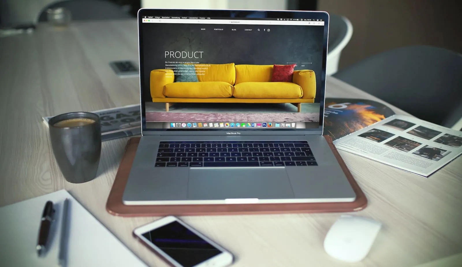 Laptop met een geopende website op een houten bureau, naast een kop koffie, een smartphone en een tijdschrift